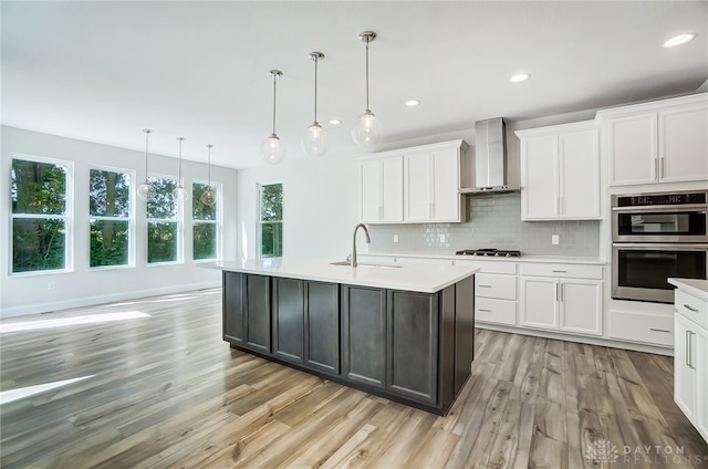 kitchen featuring light hardwood / wood-style flooring, backsplash, wall chimney exhaust hood, white cabinets, and stainless steel appliances