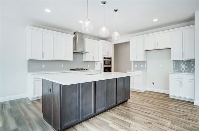 kitchen with light hardwood / wood-style floors, wall chimney range hood, white cabinetry, and tasteful backsplash