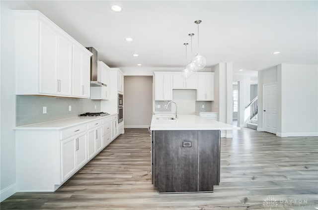 kitchen with wall chimney exhaust hood, tasteful backsplash, light hardwood / wood-style flooring, and stainless steel appliances