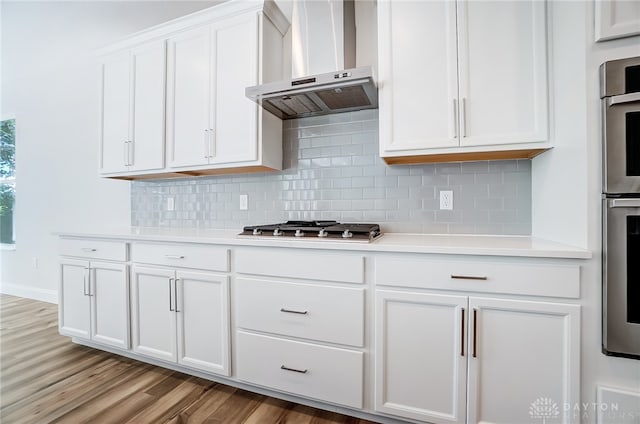 kitchen featuring wall chimney range hood, decorative backsplash, stainless steel gas cooktop, white cabinetry, and light hardwood / wood-style floors