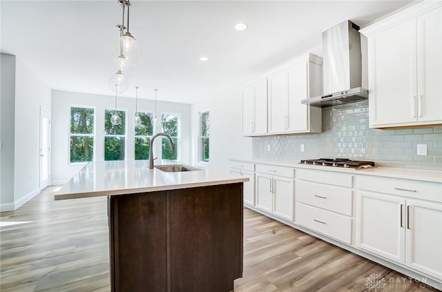 kitchen with wall chimney exhaust hood, hanging light fixtures, stainless steel gas stovetop, light hardwood / wood-style floors, and sink