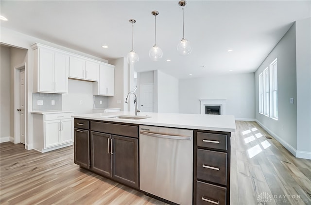 kitchen with sink, light wood-type flooring, stainless steel dishwasher, tasteful backsplash, and hanging light fixtures