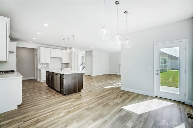 kitchen featuring light hardwood / wood-style floors, stainless steel dishwasher, a center island with sink, white cabinets, and hanging light fixtures