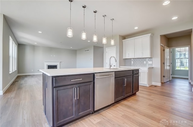 kitchen with stainless steel dishwasher, light hardwood / wood-style flooring, tasteful backsplash, white cabinetry, and sink