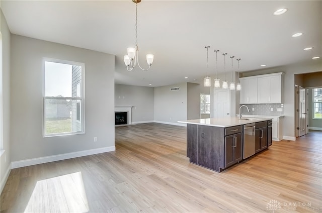 kitchen featuring backsplash, dishwasher, a center island with sink, light wood-type flooring, and white cabinets