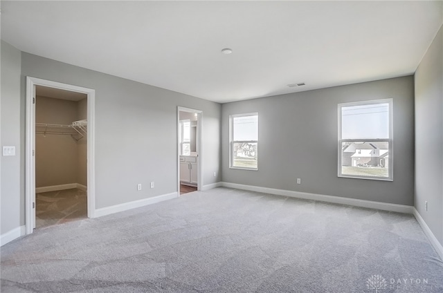 unfurnished bedroom featuring a walk in closet, carpet, multiple windows, and ensuite bath