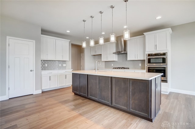 kitchen with light hardwood / wood-style flooring, backsplash, wall chimney exhaust hood, appliances with stainless steel finishes, and sink