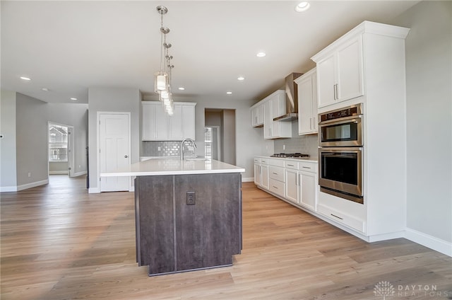 kitchen with backsplash, light wood-type flooring, white cabinetry, stainless steel appliances, and wall chimney range hood