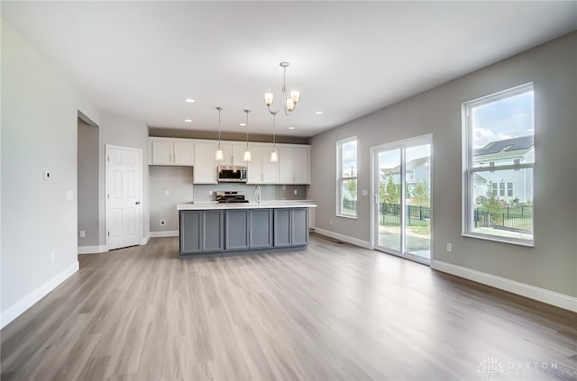 kitchen with a notable chandelier, a kitchen island with sink, light wood-type flooring, and hanging light fixtures