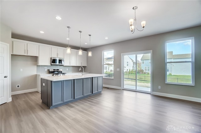 kitchen with backsplash, light wood-type flooring, appliances with stainless steel finishes, pendant lighting, and white cabinets