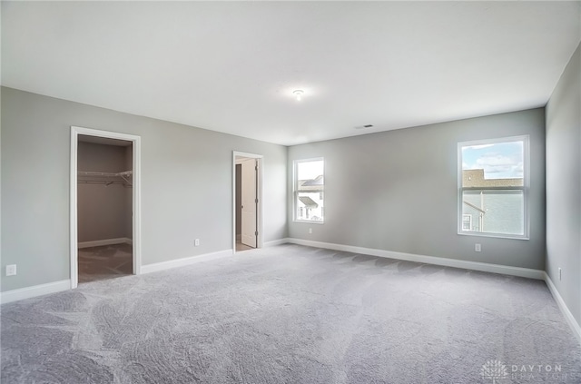 unfurnished bedroom featuring a spacious closet, carpet flooring, multiple windows, and a closet