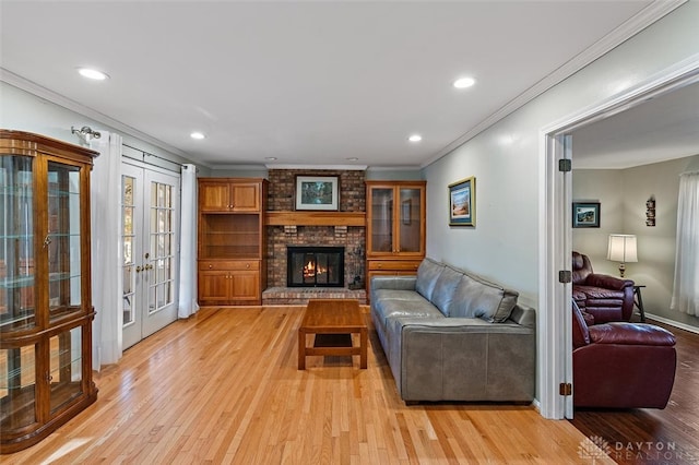 living room with crown molding, french doors, light wood-type flooring, a brick fireplace, and brick wall