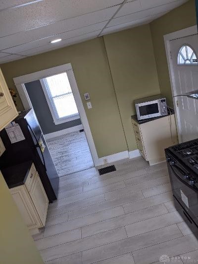 kitchen with a drop ceiling, black range, a healthy amount of sunlight, and light wood-type flooring