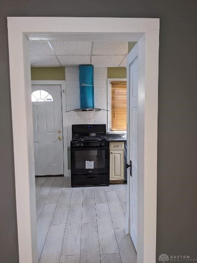 kitchen featuring decorative backsplash, black range with gas stovetop, a drop ceiling, and wall chimney range hood