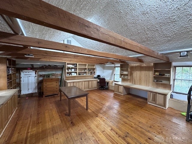 kitchen with light brown cabinetry, light wood-type flooring, built in desk, lofted ceiling with beams, and a textured ceiling