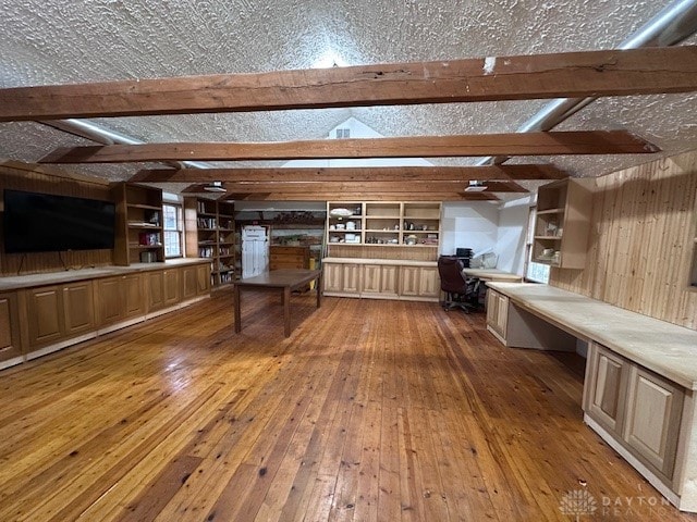 interior space featuring beamed ceiling, wooden walls, a textured ceiling, and hardwood / wood-style flooring