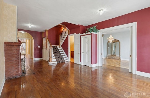 unfurnished living room featuring stairway, baseboards, arched walkways, and wood finished floors