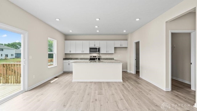 kitchen with a center island with sink, white cabinets, stainless steel appliances, and light hardwood / wood-style flooring