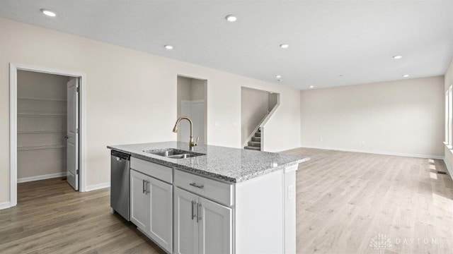 kitchen with light stone countertops, sink, stainless steel dishwasher, a center island with sink, and light wood-type flooring