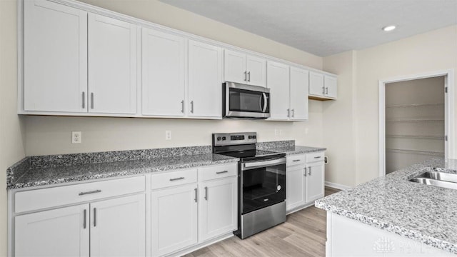 kitchen with white cabinets, sink, light hardwood / wood-style floors, light stone counters, and stainless steel appliances