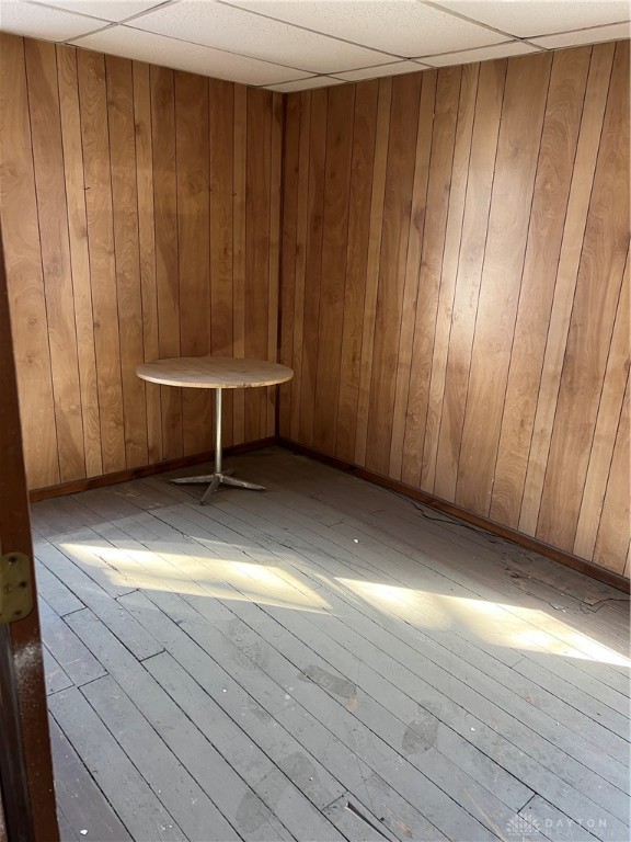 spare room featuring light hardwood / wood-style flooring, wood walls, and a drop ceiling