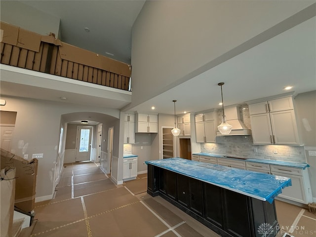 kitchen with tasteful backsplash, white cabinetry, arched walkways, baseboards, and custom exhaust hood