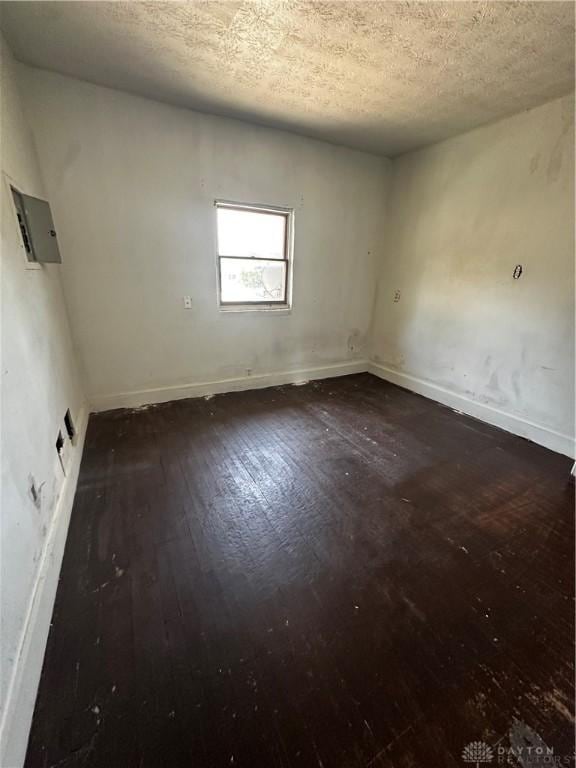 empty room featuring electric panel, dark hardwood / wood-style flooring, and a textured ceiling