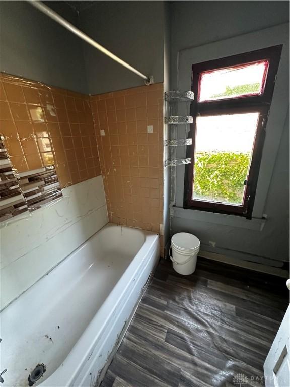 bathroom with hardwood / wood-style floors, toilet, tiled shower / bath, and tile walls