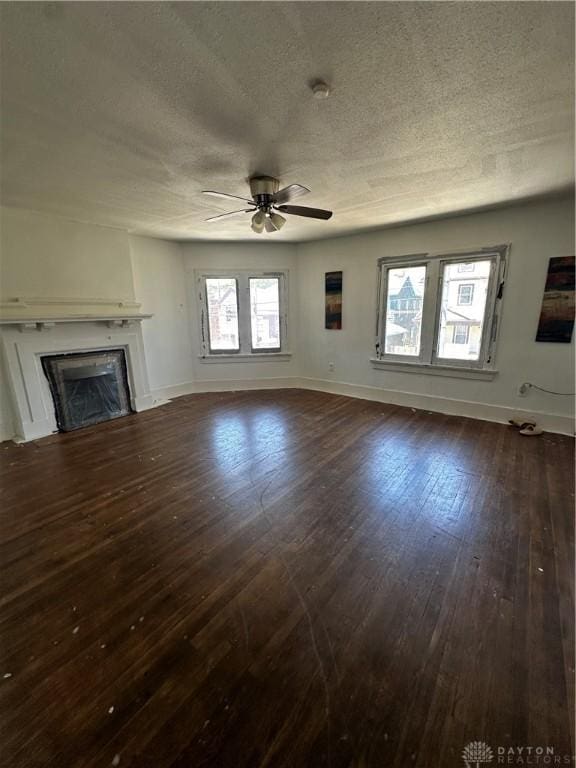 unfurnished living room featuring ceiling fan, dark wood-type flooring, and a textured ceiling