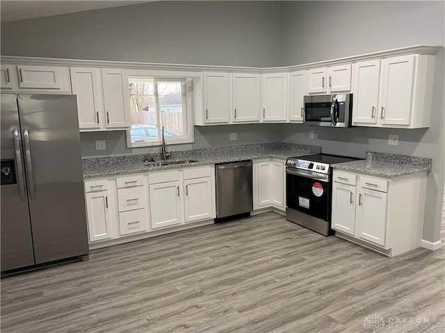 kitchen featuring lofted ceiling, sink, light hardwood / wood-style flooring, white cabinetry, and stainless steel appliances