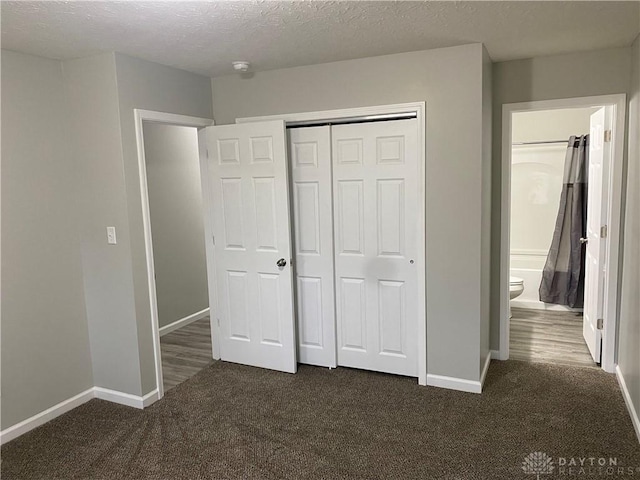 unfurnished bedroom with dark colored carpet, a textured ceiling, a closet, and connected bathroom