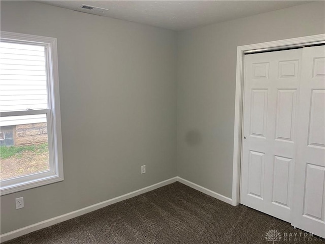 unfurnished bedroom featuring a closet, dark carpet, and multiple windows