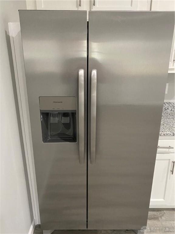 room details featuring white cabinetry, stainless steel fridge with ice dispenser, and light stone counters