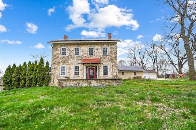 colonial house with a garage, solar panels, a chimney, and stone siding