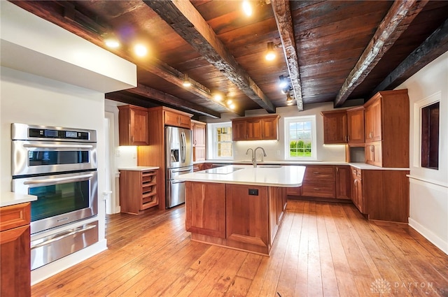 kitchen with stainless steel appliances, light hardwood / wood-style floors, a kitchen island with sink, beam ceiling, and wooden ceiling