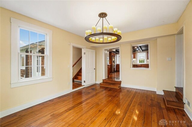 spare room featuring a healthy amount of sunlight, hardwood / wood-style floors, and a chandelier