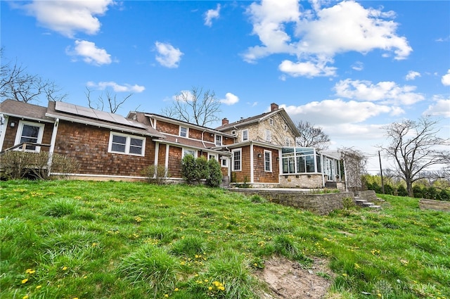 rear view of property with a sunroom and solar panels