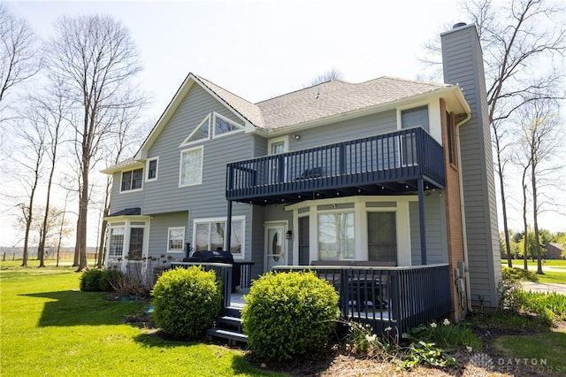 rear view of property featuring a lawn, a balcony, and a wooden deck