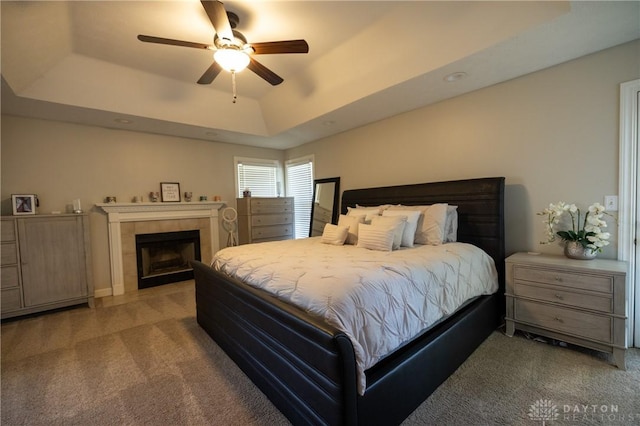 bedroom featuring a tile fireplace, ceiling fan, a tray ceiling, and carpet flooring