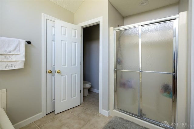 bathroom featuring toilet, a shower with door, and tile patterned floors