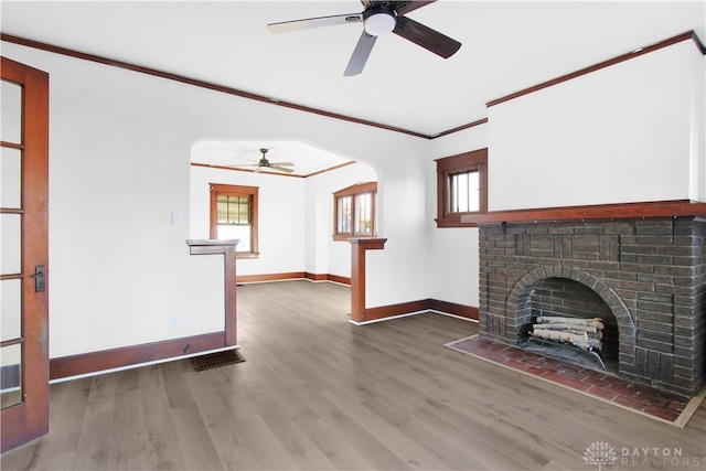 unfurnished living room with crown molding, ceiling fan, wood-type flooring, and a brick fireplace