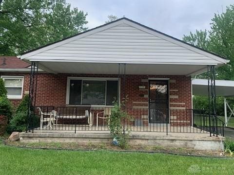 view of front of home with covered porch, a front yard, and brick siding