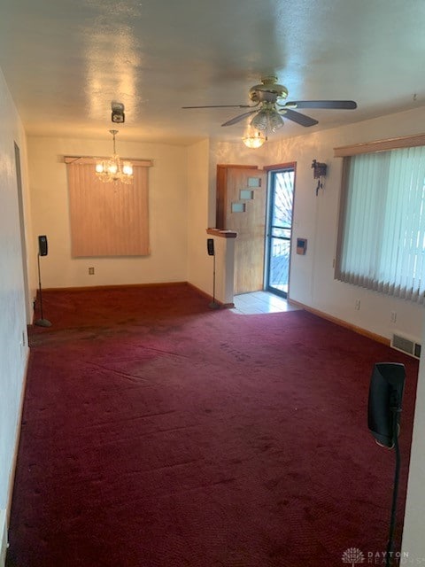 unfurnished living room with ceiling fan with notable chandelier and carpet floors