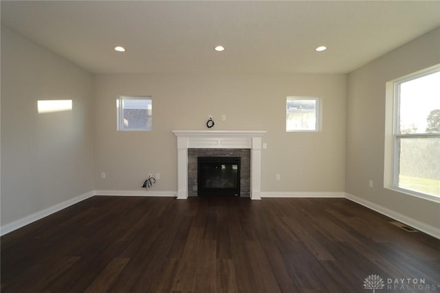 unfurnished living room featuring a healthy amount of sunlight, baseboards, dark wood-style flooring, and a glass covered fireplace