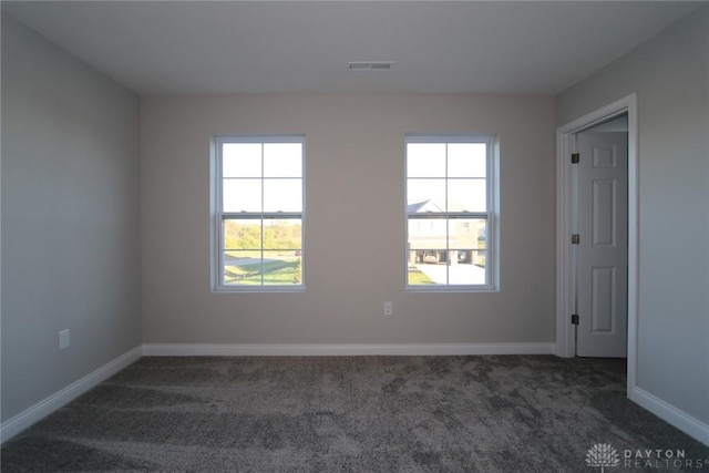 empty room featuring dark colored carpet, visible vents, and baseboards