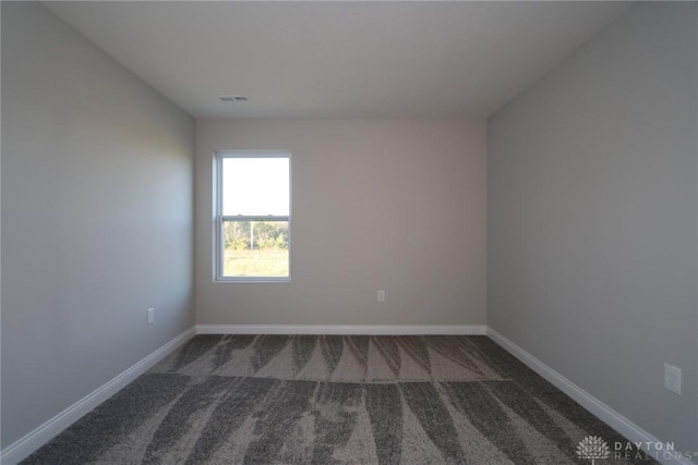 spare room featuring dark colored carpet, visible vents, and baseboards