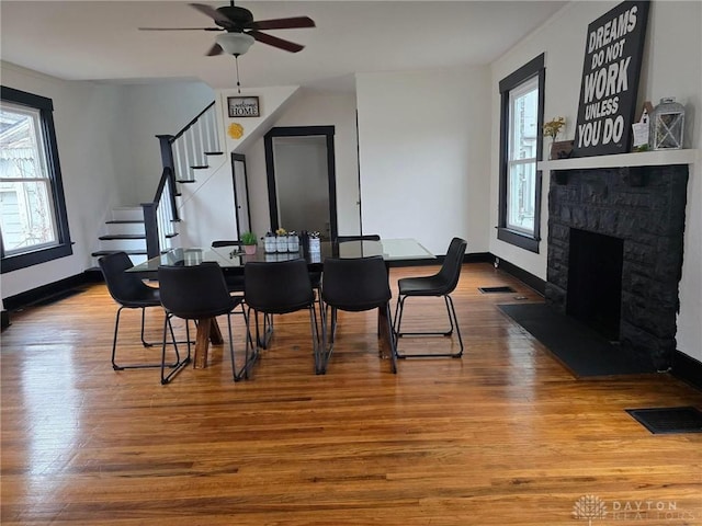 dining area with ceiling fan, a fireplace, a wealth of natural light, and hardwood / wood-style flooring