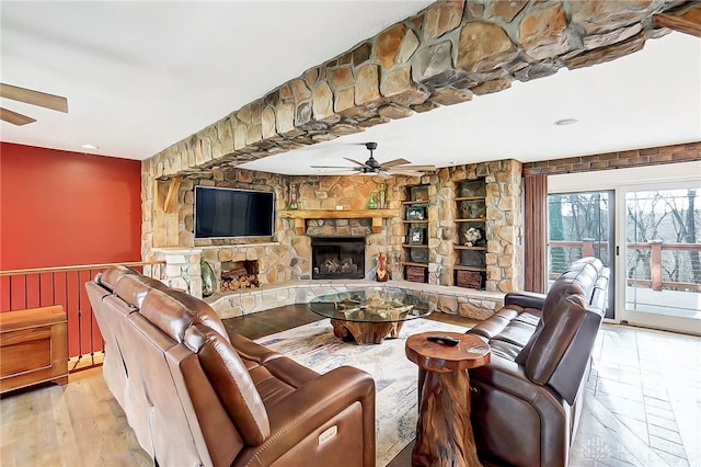 living room featuring a stone fireplace, light wood-type flooring, wooden walls, and ceiling fan