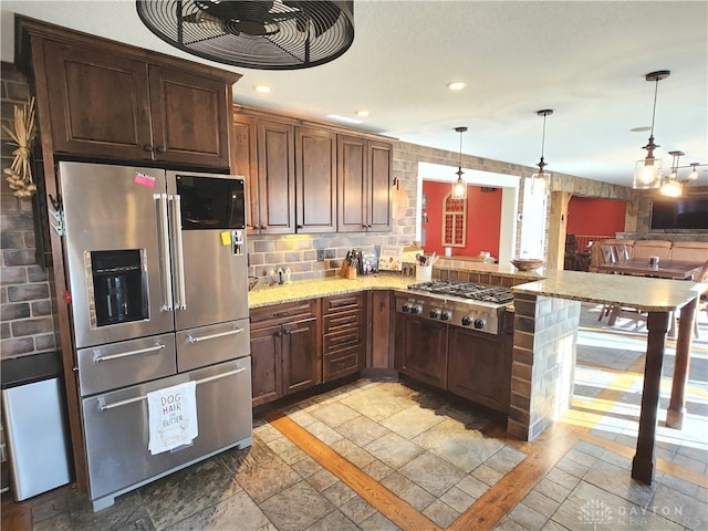 kitchen featuring light stone counters, appliances with stainless steel finishes, hanging light fixtures, a breakfast bar, and kitchen peninsula