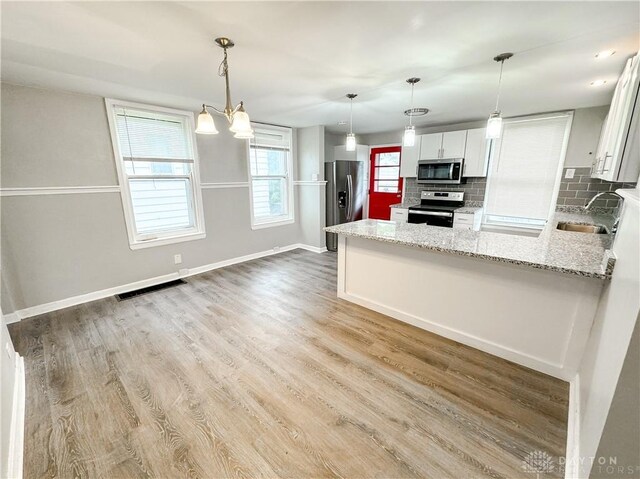kitchen with appliances with stainless steel finishes, tasteful backsplash, a sink, light stone counters, and a peninsula